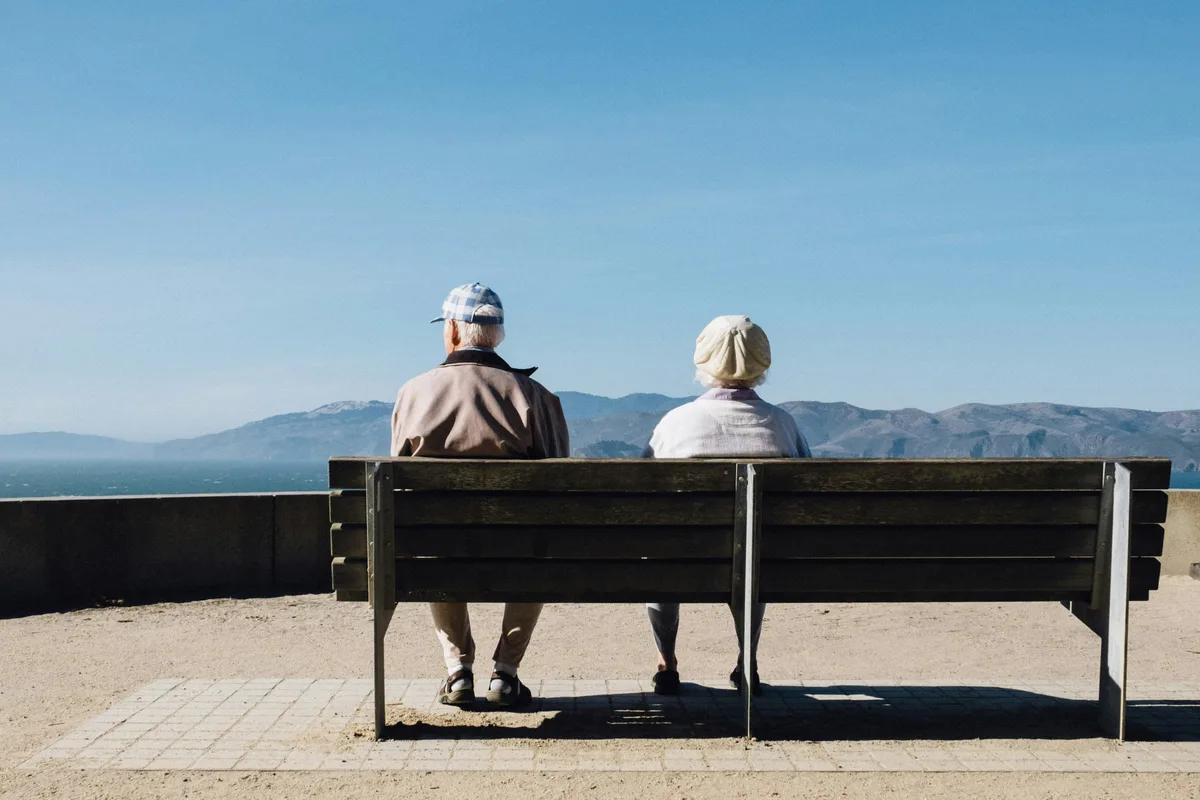Two seniors relaxing on a bench by the sea, representing Social Security retirement lifestyle in 2026